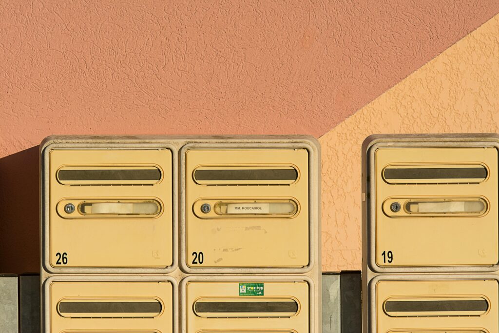 Close-up of yellow mailboxes against a textured pink wall with numbers visible.